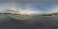 a panoramic view of an empty road in the morning sun set and the sky has clouds above it