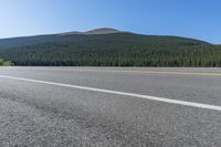 a road is empty and the trees are green behind it and there is a hill in the background