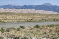 an open desert with a large mountains in the background a road is empty and there is a sign in the foreground that says