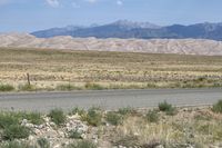 an open desert with a large mountains in the background a road is empty and there is a sign in the foreground that says