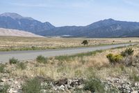 an open desert with a large mountains in the background a road is empty and there is a sign in the foreground that says