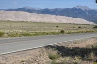 an open desert with a large mountains in the background a road is empty and there is a sign in the foreground that says