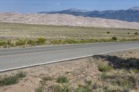 an open desert with a large mountains in the background a road is empty and there is a sign in the foreground that says