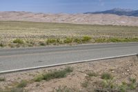 an open desert with a large mountains in the background a road is empty and there is a sign in the foreground that says