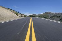 an empty road is lined with a mountain and trees in the background, with a blue sky above