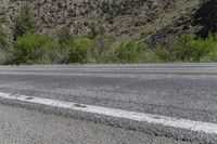 an empty road has trees and mountains near by it and a stop sign on the side of it