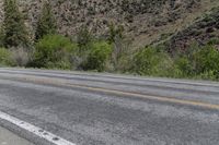 an empty road has trees and mountains near by it and a stop sign on the side of it