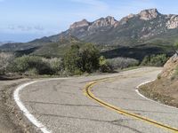 an empty road near two yellow lines that go through the center of the curve on the mountain