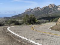 an empty road near two yellow lines that go through the center of the curve on the mountain