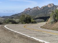 an empty road near two yellow lines that go through the center of the curve on the mountain