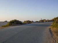 an empty road in the desert with no traffic on it, on the beach with many shrubs