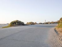 an empty road in the desert with no traffic on it, on the beach with many shrubs