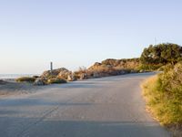 an empty road in the desert with no traffic on it, on the beach with many shrubs