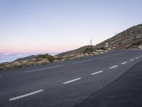 an empty winding road on a mountain with the sun set above the mountains in the background