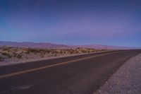 empty road in an arid area with mountain range in background at dusk time during sunset