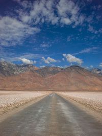 an empty road leads through the desert with mountains in the background in the distance, and clouds