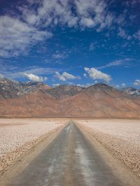 an empty road leads through the desert with mountains in the background in the distance, and clouds