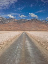 an empty road leads through the desert with mountains in the background in the distance, and clouds