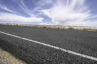 an empty road in the desert with a sky full of clouds behind it and a line in the foreground