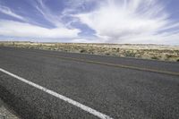 an empty road in the desert with a sky full of clouds behind it and a line in the foreground