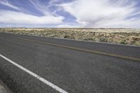 an empty road in the desert with a sky full of clouds behind it and a line in the foreground