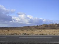 an empty road in the middle of a desert area with a blue sky overhead and white clouds above it