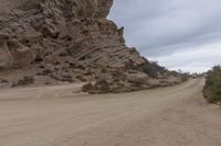 an empty road next to a rocky wall in the desert, with trees and rocks all around