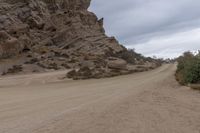 an empty road next to a rocky wall in the desert, with trees and rocks all around