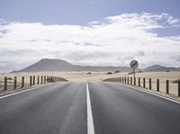 an empty road leads down to the desert landscape with mountain in background and a fence separating it