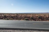 a desert with a road that is empty on the side of it with a hill and mountains in the background