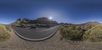 a view from a fisheye lens of an empty road in the desert, with a sun and mountain