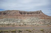 a car driving along an empty road in the desert outside of an arid area with cliffs and bushes