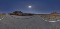 a fisheye panoramic image of an empty road in the desert with mountains and a bright blue sky