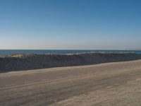 a person riding a bike down an empty road near the ocean in a sunny day