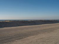 a person riding a bike down an empty road near the ocean in a sunny day