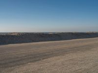 a person riding a bike down an empty road near the ocean in a sunny day