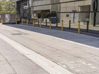 the side of an empty road is covered by fencing and parking meters as a man rides his scooter down it