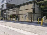 the side of an empty road is covered by fencing and parking meters as a man rides his scooter down it