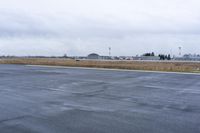 an empty street on the side of a field in the rain with an airplane landing