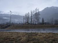 the mountains are foggy and in the distance is snow and grass and there is an empty road