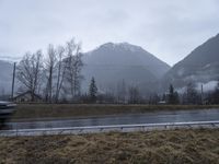 the mountains are foggy and in the distance is snow and grass and there is an empty road