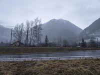 the mountains are foggy and in the distance is snow and grass and there is an empty road