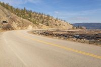 an empty road in the middle of a forest area with water and mountains behind it