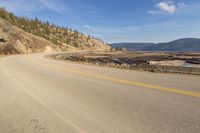 an empty road in the middle of a forest area with water and mountains behind it