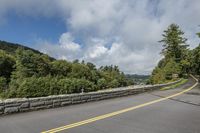 the road is empty and the trees are green with mountains in the background under the blue sky