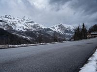 the road is empty near the mountain side with snow on it and there are no cars parked in it