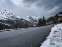 the road is empty near the mountain side with snow on it and there are no cars parked in it