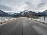 empty road with mountain in distance under cloudy sky and metal railings in foreground