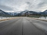 empty road with mountain in distance under cloudy sky and metal railings in foreground