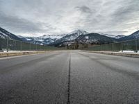 empty road with mountain in distance under cloudy sky and metal railings in foreground